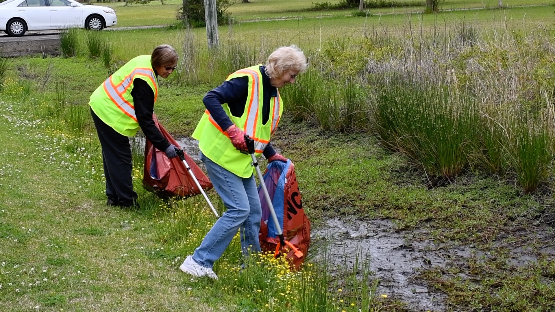 two ladies picking up trash on side of road