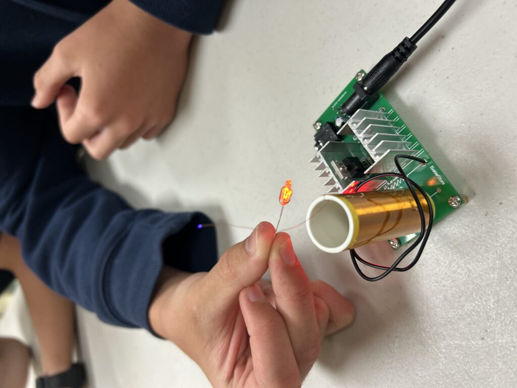 Child demonstrating a mini Tesla coil by holding a small light near it to show how the light activates wirelessly.