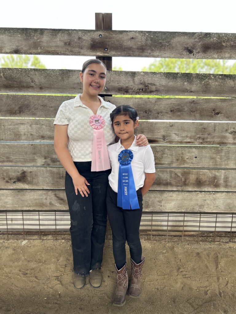 Sabella Rodgers and Victoria Vargas posing together with their sixth and first place ribbons after the dairy show